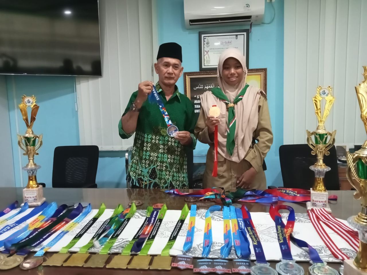 MEDALI -.Siswi SMP Muhammadiyah 2 Taman (SPEMDUTA) Sidoarjo, Zahrah Inas Fawza yang duduk di bangku kelas VII menorehkan berbagai prestasi dengan menyabet berbagai medali didamping Kepala Spemduta, Zainal Arif Fakhrudi, Rabu (04/06/2025).
