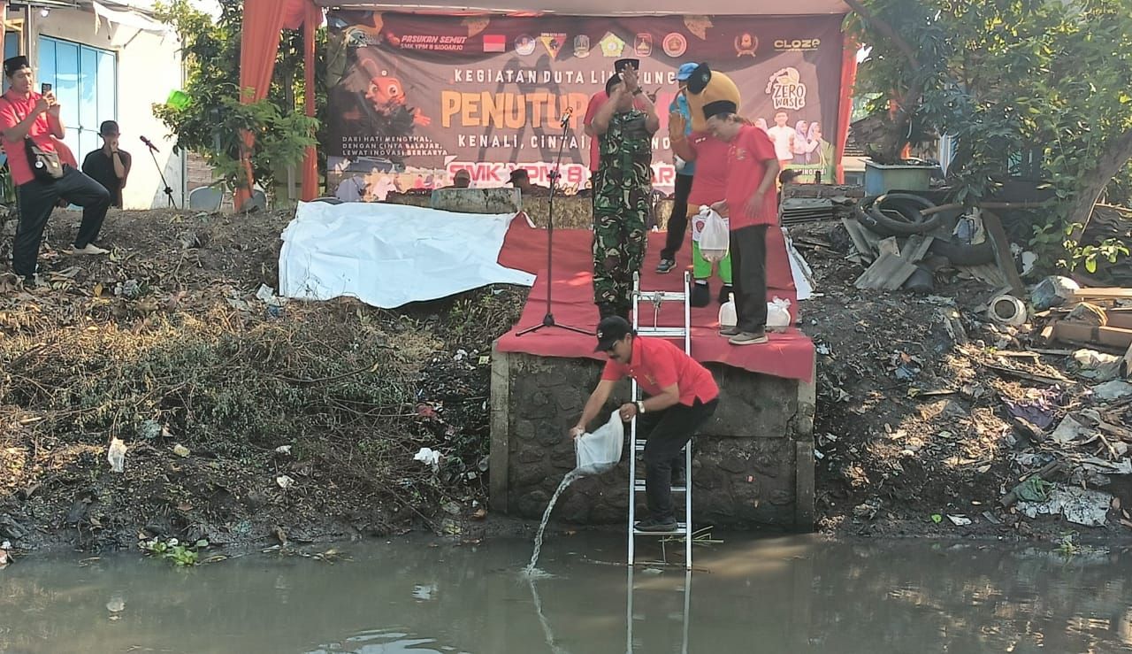 TABUR - Ketua Yayasan YPM Achmad Makki memulai menabur benih ikan 17.750 ekor ke Sungai Anggaswangi, Kecamatan Sukodono, Sidoarjo sebagai tanda penutupan MPLS di SMK YPM 8 Sidoarjo yang diisi membersihkan sungai dan menabur benih ikan, Jumat (18/07/2025).