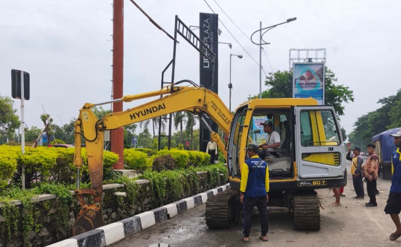 BERSIHKAN SALURAN - Dinas Pekerjaan Umum Bina Marga dan Sumber Daya Air (PUBM dan SDA) Sidoarjo menerjunkan alat berat untuk menormalisasi saluran air (drainase) di sekitar Lippo Plaza Sidoarjo agar tidak terjadi banjir, Rabu (12/11/2025).