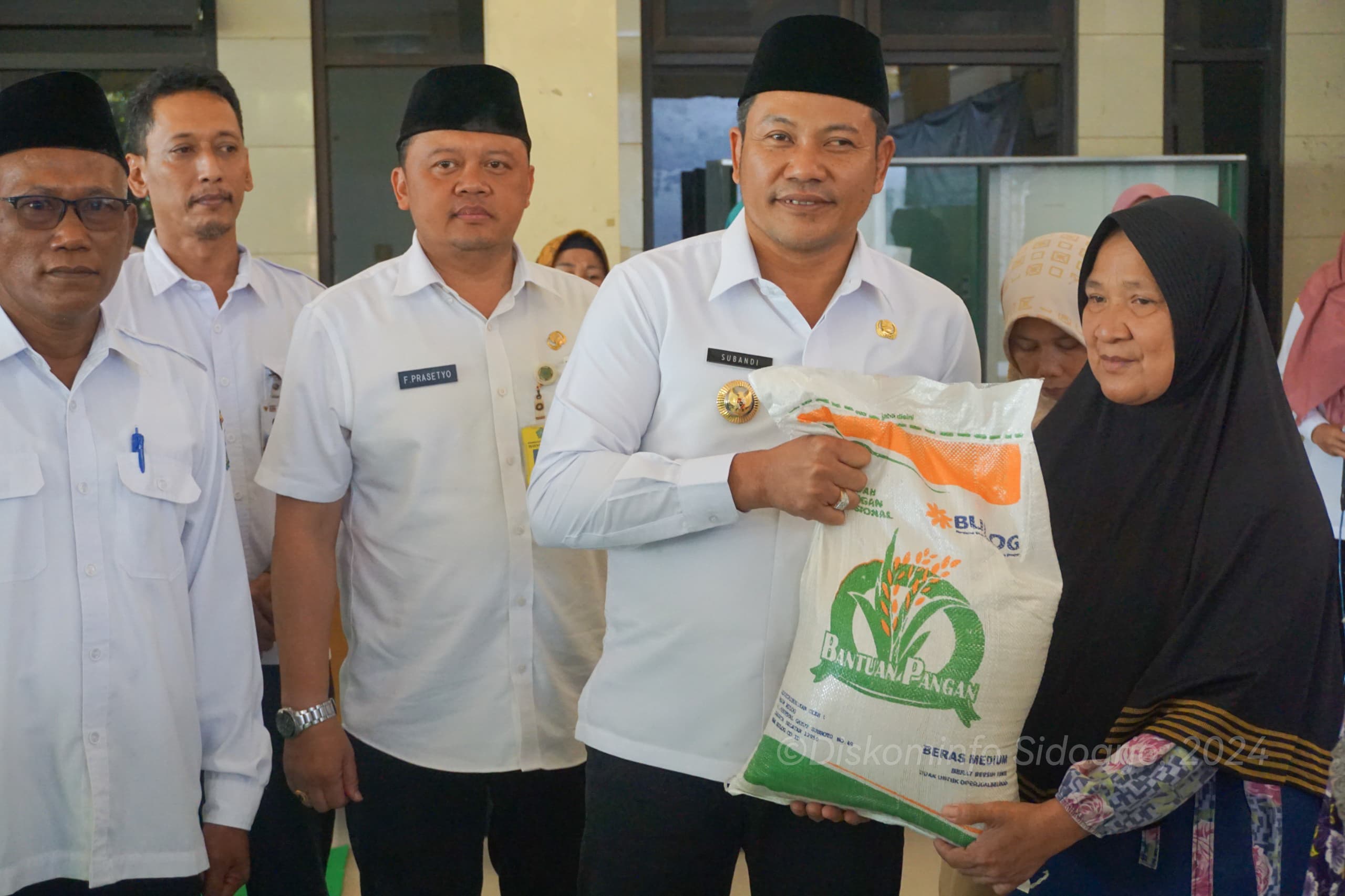 SERAHKAN - Plt Bupati Sidoarjo Subandi menyerahkan bantuan beras 10 kilogram untuk keluarga miskin yang ada di empat desa di Kecamatan Prambon salah satunya di Desa Simogirang, Kecamatan Prambon, Sidoarjo, Rabu (12/06/2024).