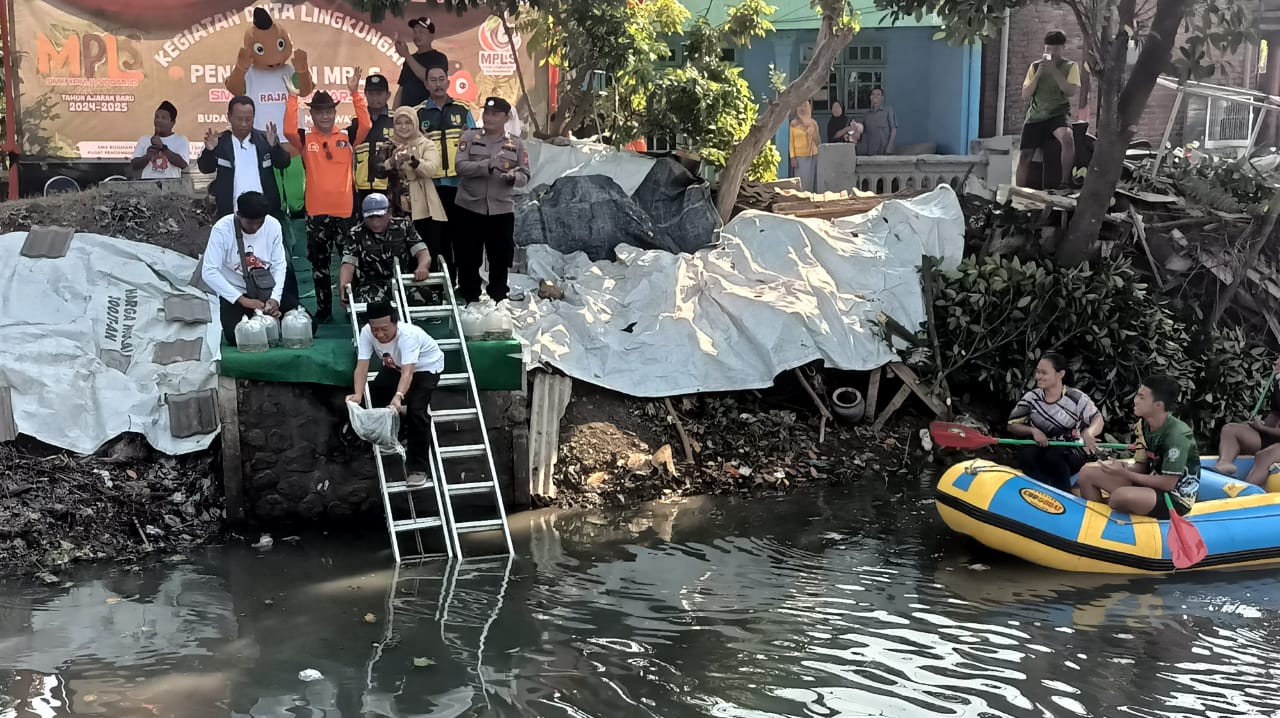 TEBAR - Waka Kurikulum SMK YPM 8 Sidoarjo, Afthoni ST MM memimpin prosesi penebaran benih ikan nila dan lele ke Sungai Desa Anggaswangi, Kecamatan Sukodono usai dibersihkan sekitar 600 siswa baru saat penutupan Masa Pengenalan Lingkungan Sekolah (MPLS), J