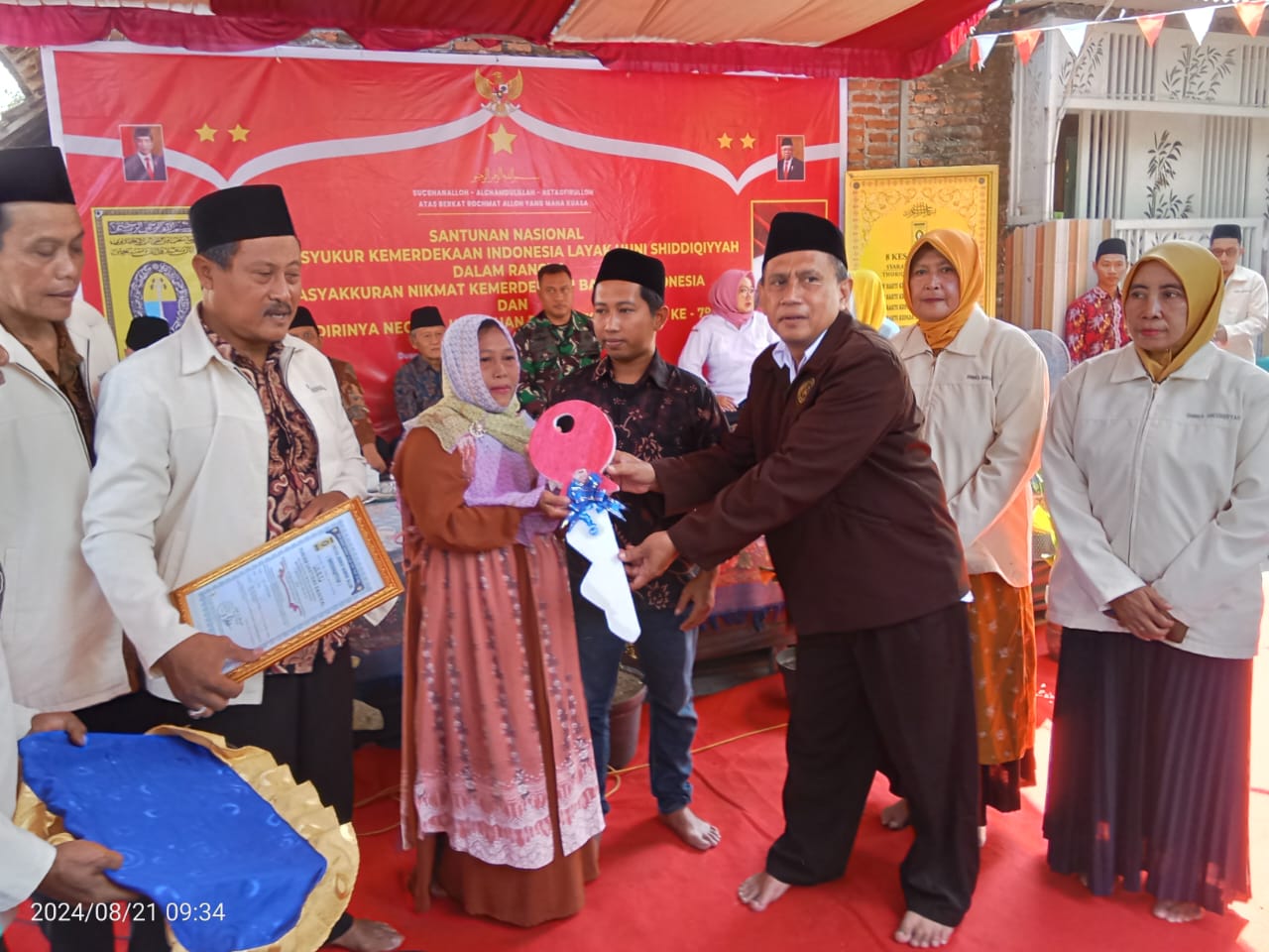 SERAHKAN - Ketua Panitia Pembangunan Rumah Layak Huni Jamaah Thoriqoh Shiddiqiyyah, Bambang Parikeno menyerahkan kunci rumah yang baru dibangun secara simbolis kepada Sukesi dan putranya Syaifuddin bersama relawan, Rabu (21/08/2024).