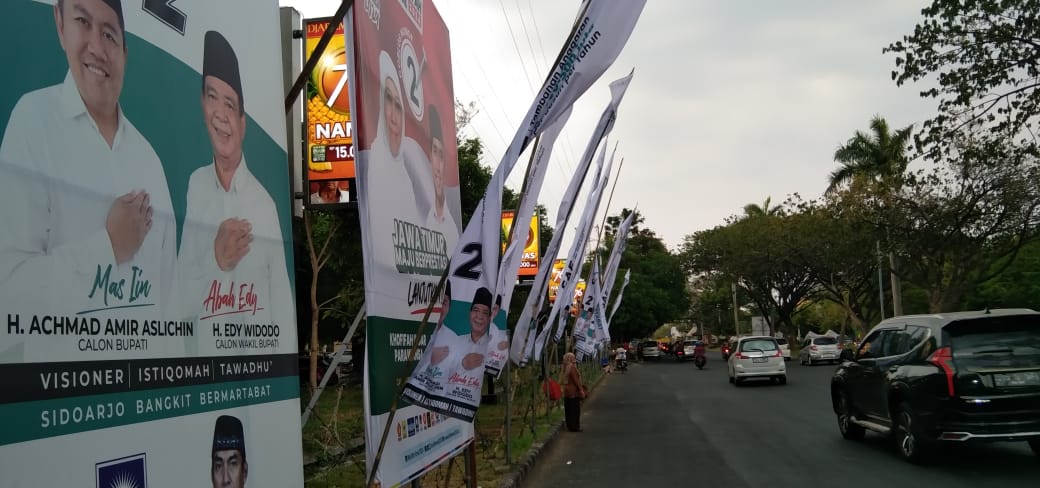 PASANG - Komisi Pemilihan Umum (KPU) Sidoarjo mulai memasang Alat Peraga Kampanye (APK) Paslon Pilkada 2024 di sejumlah itik wilayah perkotaan maupun pedesaan di wilayah Sidoarjo, Jumat (18/10/2024).