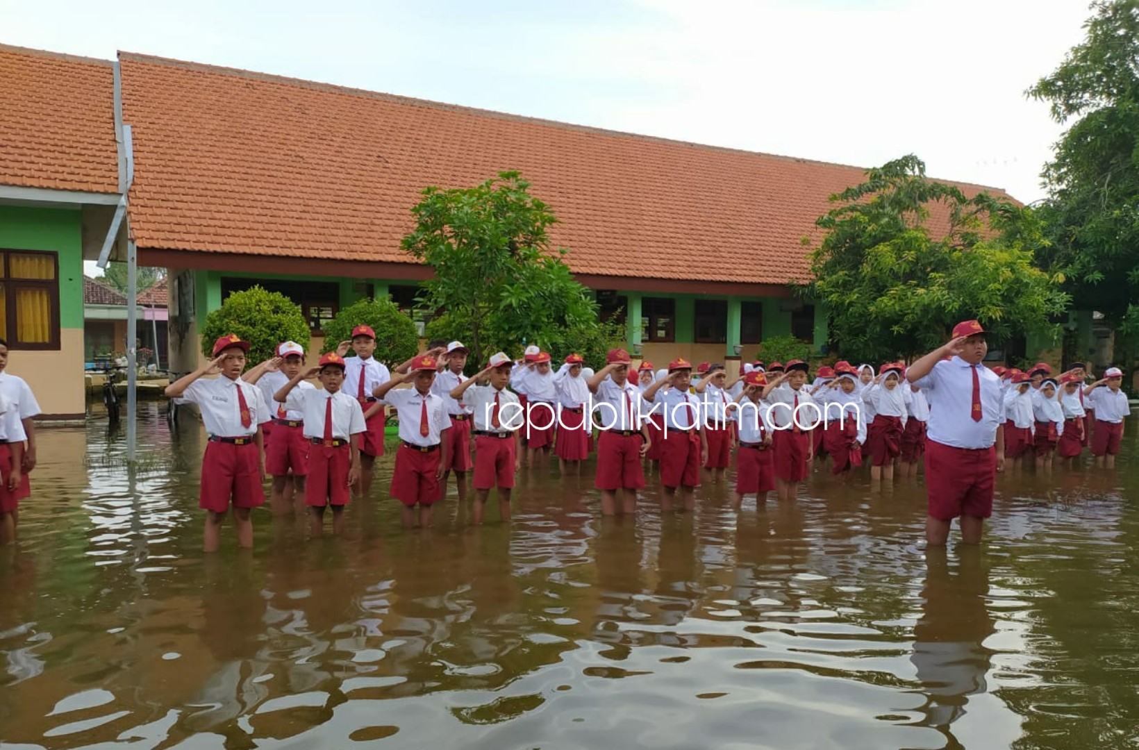 BANJIR - Para siswa dan siswi SDN Banjarasri, Kecamatan Tanggulangin, Sidoarjo tetap menggelar upacara bendera meski halaman sekolah mereka tenggenang air banjir selama dua pekan terakhir, Senin (10/02/2020).