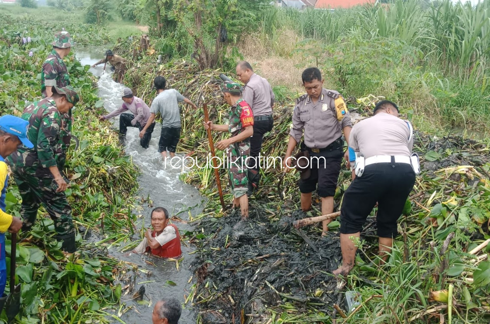 BERSIHKAN - Sejumlah warga bersama anggota Polsek dan Koramil Wonoayu membersihkan saluran air di Desa Semambung, Kecamatan Wonoayu, Sidoarjo agar air banjir segera surut, Kamis (05/03/2020).