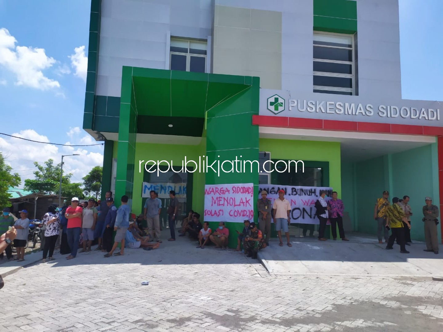 TOLAK - Puluhan warga Desa Sidodadi, Kecamatan Candi, Sidoarjo membentangkan sejumlah poster penolakan Puskesmas Sidodadi dijadikan ruang perawatan isolasi korban Covid-19, Selasa (31/03/2020).