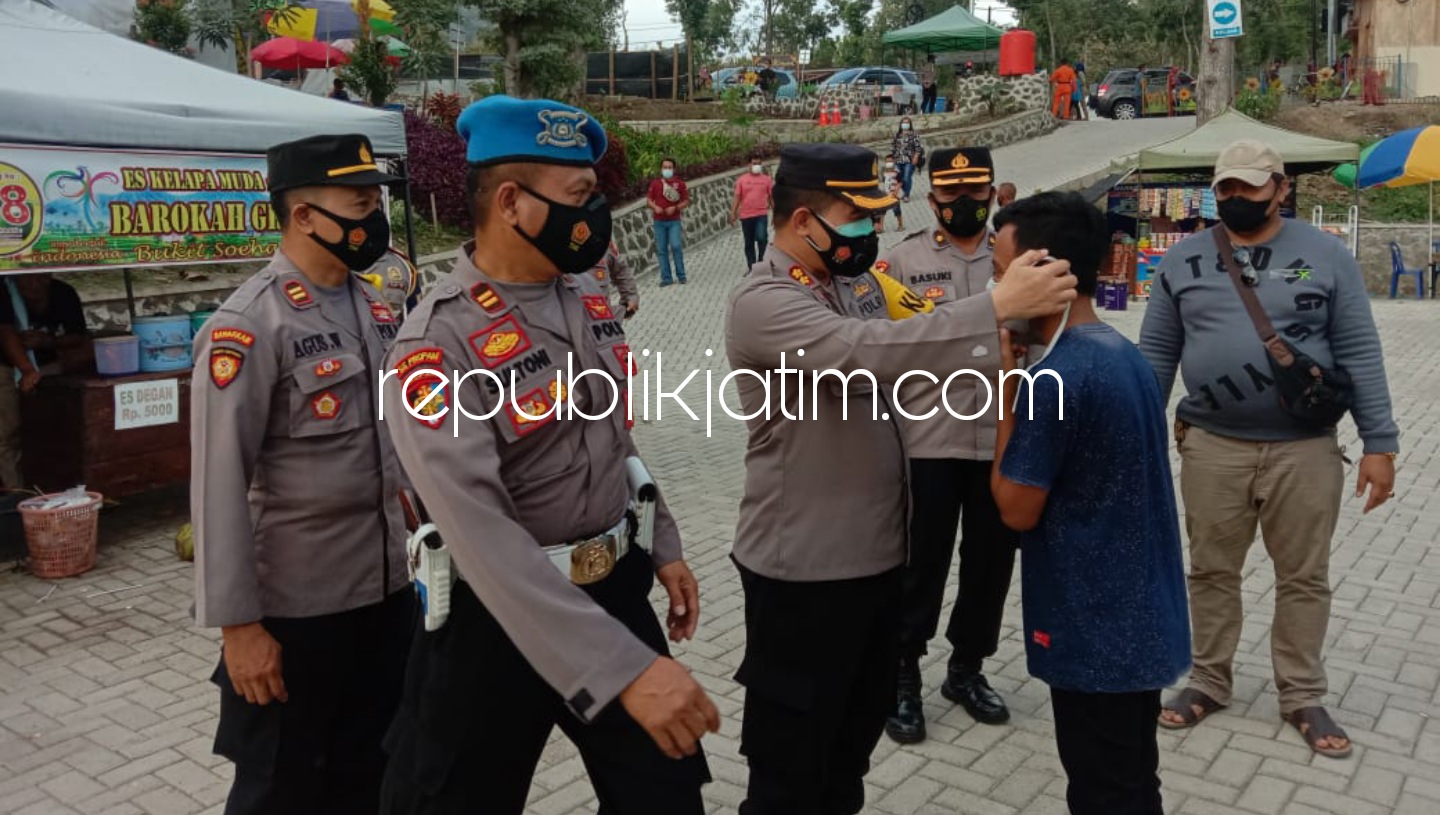 KENAKAN - Kapolres Ponorogo AKBP Mochamad Nur Azis membagikan dan mengenakan masker kepada pengunjung di dua lokasi wisata di Desa Biting, Kecamatan Badegan, Ponorogo yang tak jauh dari lokasi Pos Penyekatan, Sabtu (22/05/2021).