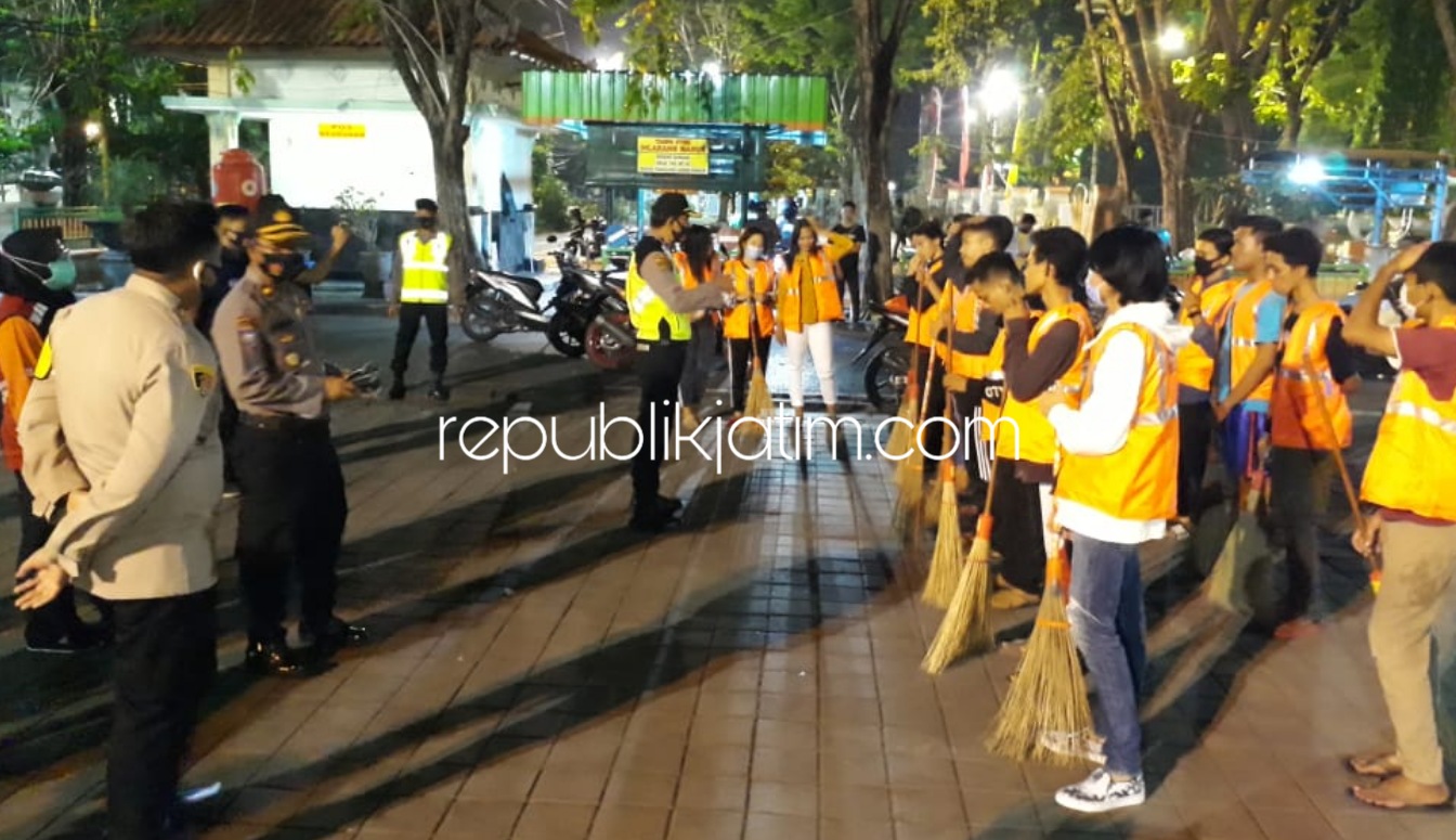 MENYAPU - Puluhan pemuda pelanggar yang tak memakai masker saat dikeramaian disanksi menyapu Alun-Alun Sidoarjo, Jumat (28/09/2020) malam.