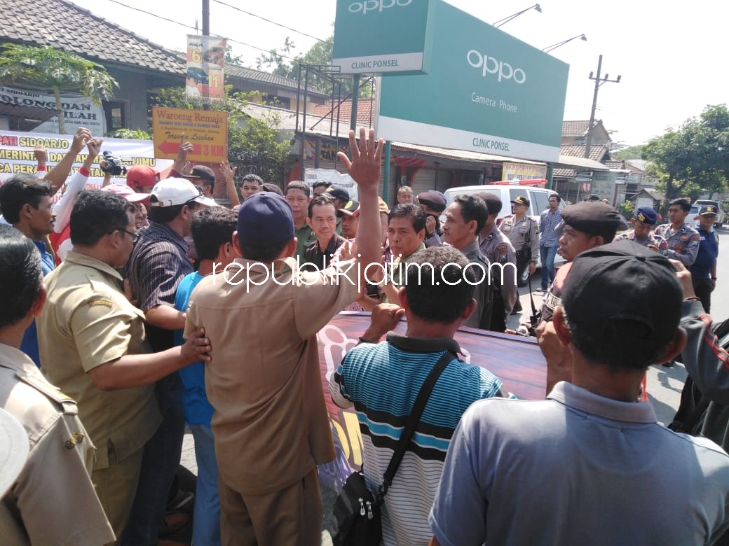 DIHADANG - Petugas juru sita Pengadilan Negeri Sidoarjo, Sambodo Raharjo dihadang warga Desa/Kecamatan Krembung saat eksekusi lahan aset desa dengan dikawal ketat petugas kepolisian, Selasa (04/09/2018).