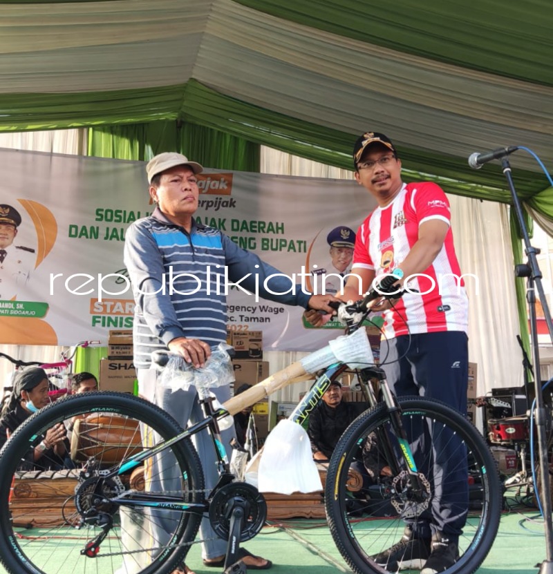 HADIAH - Bupati Sidoarjo, Ahmad Muhdlor Ali menyerahkan hadiah Warga Desa Wage, Kecamatan Taman, Sidoarjo, Muhammad Wujud berupa sepeda Gunung saat Jalan Sehat di Balai Desa Wage, Kecamatan Taman, Sidoarjo, Minggu (12/12/2022).
