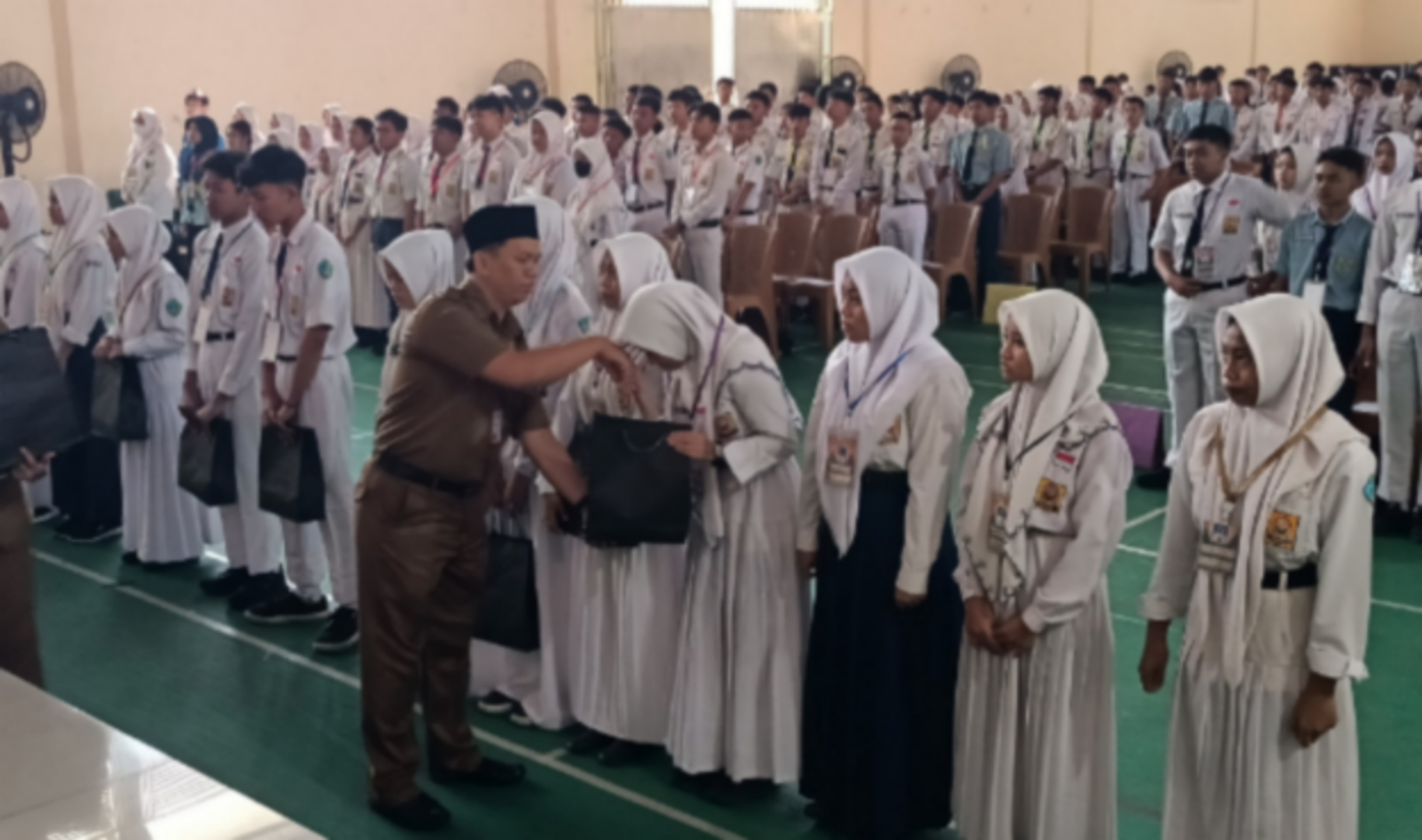 SERAGAM GRATIS - Waka Kesiswaan SMAN 4 Sidoarjo, Nunung Prasetyo menyerahkan seragam gratis untuk siswa baru SMAN 4 Sidoarjo di Gedung Serba Guna saat mengikuti apel bersama pembukaan MPLS se Jatim di Aula SMAN 4 Sidoarjo, Senin (15/07/2024).