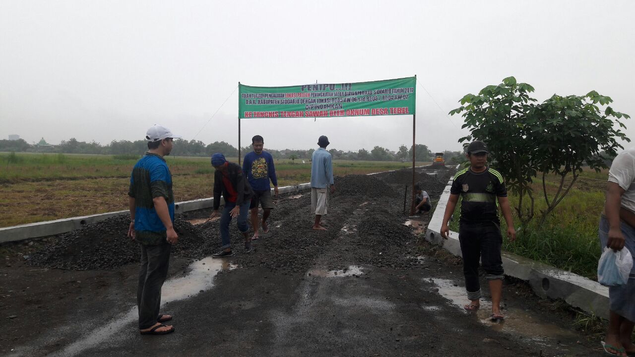TOLAK PEMBANGUNAN - Belasan warga Desa Tebel, Kecamatan Gedangan, Kabupaten Sidoarjo menolak proyek pembangunan jalan tembus Desa Tebel menuju Desa Punggul dengan memasang spanduk di lokasi proyek, Jumat (24/11/2017).